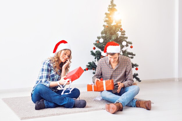 Concepto de vacaciones, Navidad y familia - Joven pareja feliz abriendo regalos en casa.