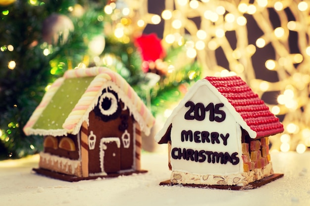 concepto de vacaciones, navidad, repostería y dulces - cierre de hermosas casas de pan de jengibre en la mesa sobre fondo de luces