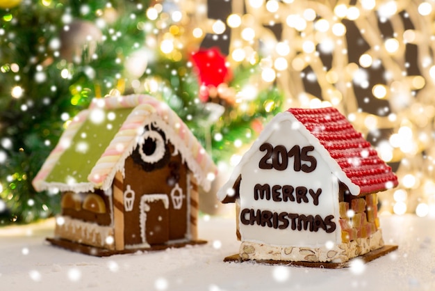 concepto de vacaciones, navidad, repostería y dulces - cierre de hermosas casas de pan de jengibre en la mesa sobre fondo de luces