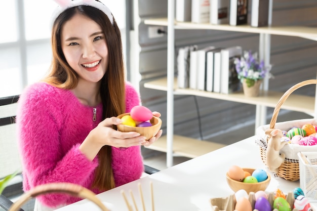 Concepto de vacaciones de Pascua, feliz espectáculo de mujer joven asiática sosteniendo una canasta con coloridos huevos de Pascua en el fondo de la habitación blanca