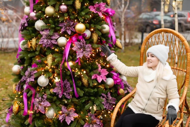 Concepto de vacaciones y personas - mujer joven en ropa de invierno sobre el árbol de navidad