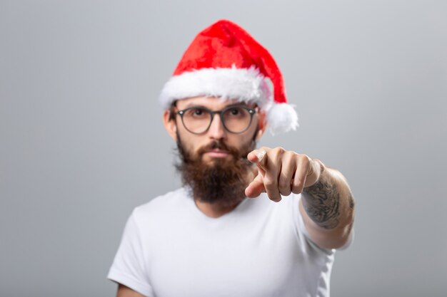 Concepto de vacaciones y personas - retrato de un hombre brutal guapo con sombrero de Navidad. Sobre fondo gris.