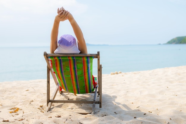 Concepto de vacaciones en la playa de verano Mujer de Asia con sombrero relajante y brazo arriba en la playa de sillas en Tailandia