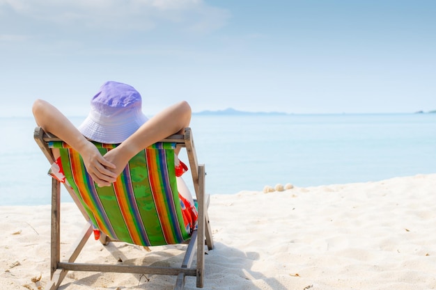 Concepto de vacaciones en la playa de verano Mujer de Asia con sombrero relajante y brazo arriba en la playa de sillas en Tailandia