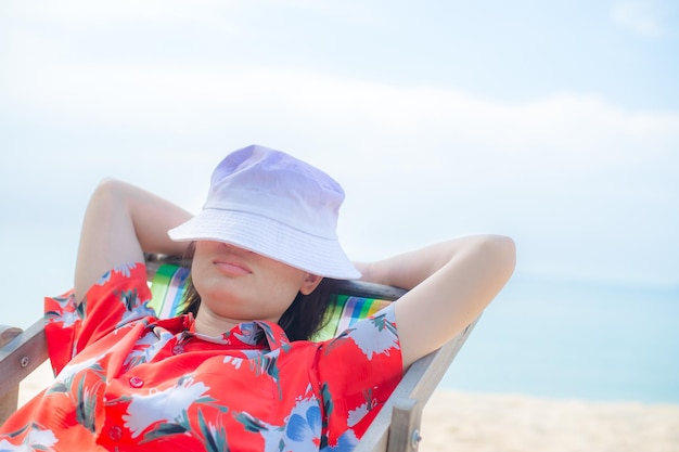 Concepto de vacaciones en la playa de verano Mujer de Asia con sombrero relajante y brazo arriba en la playa de sillas en Tailandia