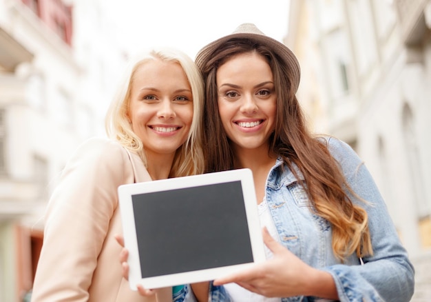 concepto de vacaciones, publicidad, tecnología y turismo: dos hermosas chicas toursits con tablet pc de pantalla en blanco en la ciudad