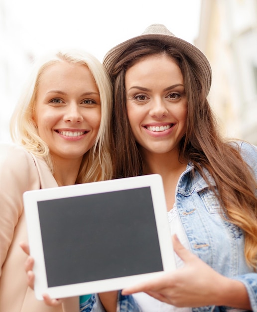 concepto de vacaciones, publicidad, tecnología y turismo: dos hermosas chicas toursits con tablet pc de pantalla en blanco en la ciudad