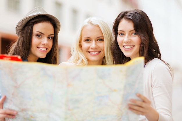 concepto de vacaciones y turismo - chicas guapas que buscan en el mapa turístico de la ciudad