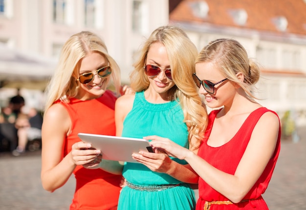 concepto de vacaciones y turismo - hermosas chicas rubias turistas mirando hacia la tableta en la ciudad