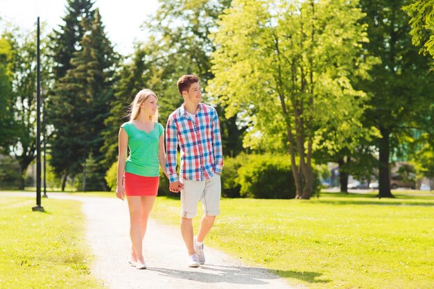 concepto de vacaciones, vacaciones, amor y amistad - pareja sonriente caminando y tomándose de la mano en el parque