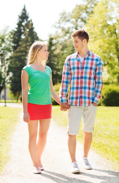 concepto de vacaciones, vacaciones, amor y amistad - pareja sonriente caminando y tomándose de la mano en el parque