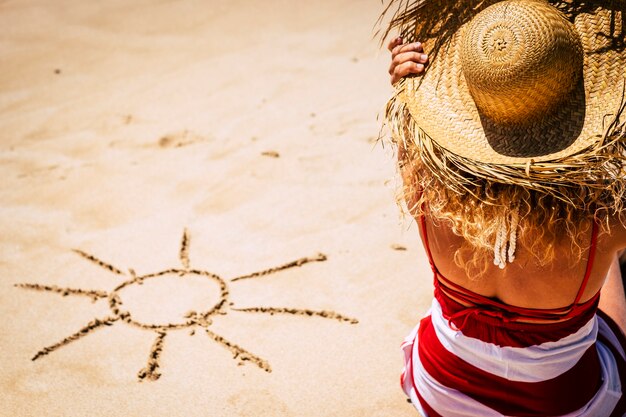 Concepto de vacaciones de vacaciones de verano con niña sentada en la playa y sol deisgned en la arena