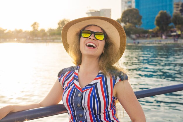 Concepto de vacaciones, vacaciones, viajes y personas de verano - sonriente mujer joven riendo con gafas de sol y sombrero en la playa sobre el fondo del mar.