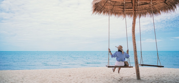 Concepto de vacaciones de verano Mujer joven con elegante vestido azul y sombrero de paja con cielo azul en la playa.