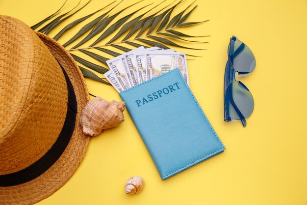 Concepto de vacaciones de verano. Pasaporte con dinero, gafas de sol y sombrero en mesa amarilla