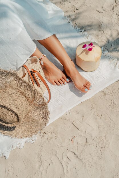 Concepto de vacaciones de verano Pies y sombrero de paja con cocos en la arena de la playa