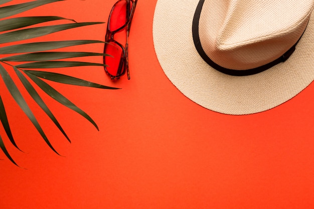 Concepto de vacaciones de verano. Sombrero de hombre, gafas de sol y rama de palma sobre un fondo coral brillante