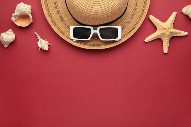 Foto concepto de vacaciones de viaje sombrero con gafas de sol y conchas marinas sobre fondo rojo espacio para texto