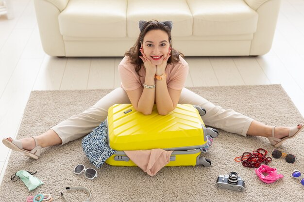 Concepto de vacaciones, viaje y viaje: la mujer joven recoge una maleta en casa en el dormitorio, muchas cosas, vacaciones y una maleta amarilla.