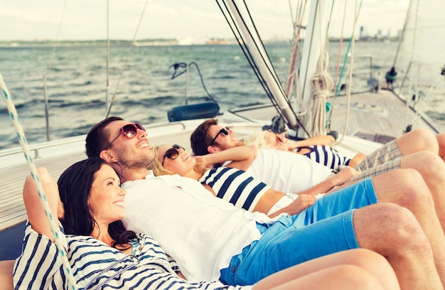 concepto de vacaciones, viajes, mar, amistad y personas - amigos sonrientes acostados en la cubierta del yate