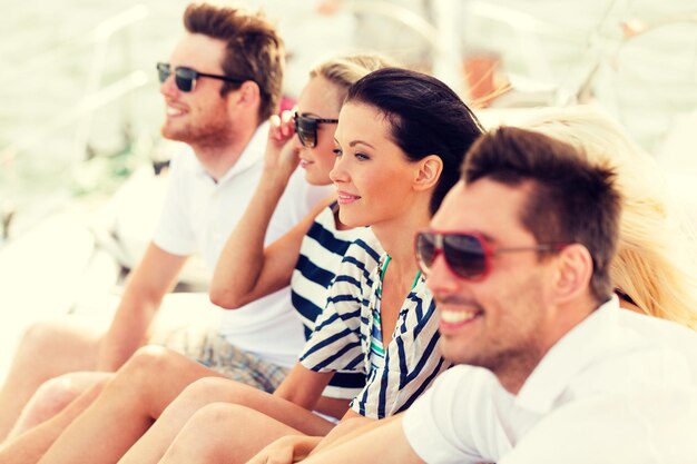 concepto de vacaciones, viajes, mar, amistad y personas - amigos sonrientes sentados en la cubierta del yate