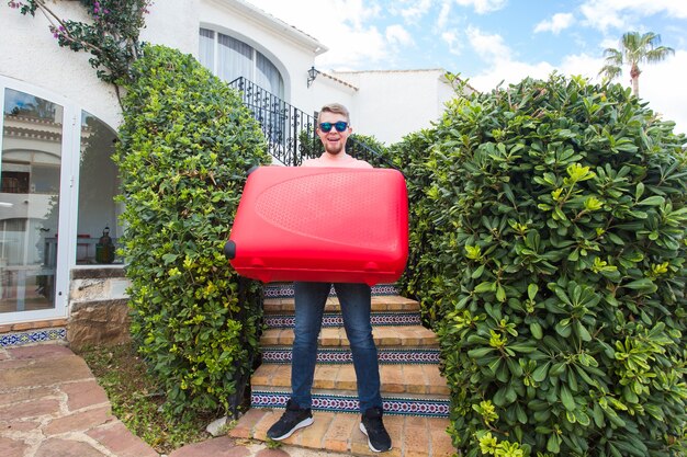 Concepto de vacaciones, viajes y turismo. Hombre guapo con maleta roja de pie sobre una escalera.