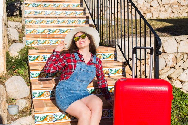 Concepto de vacaciones, viajes y turismo. mujer joven con maleta roja sentada en una escalera.