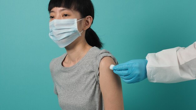 Concepto de vacuna. Mujer esperando la inyección de la vacuna contra el coronavirus por parte del médico. Mujer asiática con máscara médica abra el hombro y la parte superior del brazo sobre fondo verde azul. Esperando la vacunación.