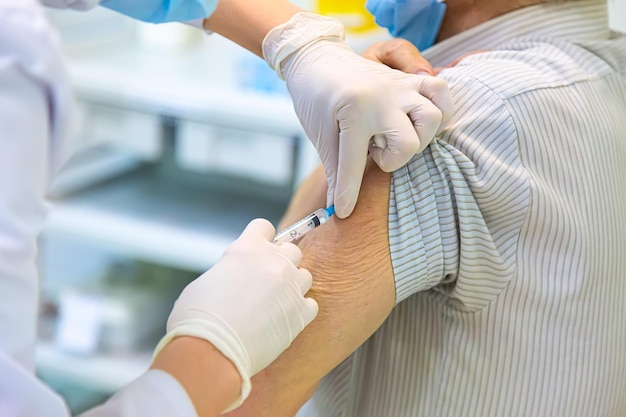 Concepto de vacunación COVID-19. Doctor en guantes de goma inyectando una jeringa con vacuna. Cierre con enfoque selectivo.