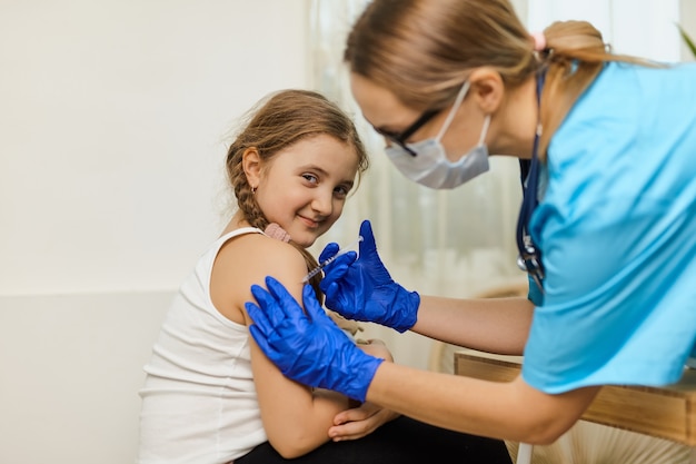 Foto el concepto de vacunación. doctora vacunando a niña linda en la clínica