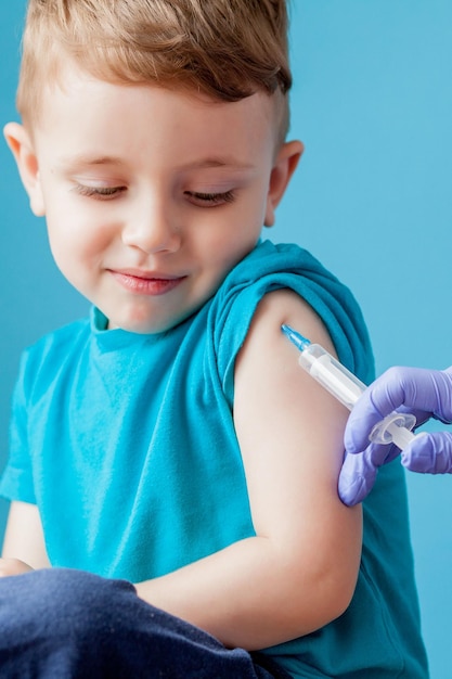 Foto concepto de vacunación doctora vacunando a un niño lindo sobre fondo azul de cerca
