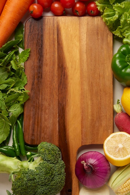 Concepto vegetal la tabla de cortar de madera rodeada de varias verduras en la mesa.