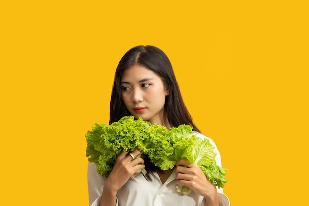 Concepto vegetariano Mujer sana con camisa blanca sostenga lechuga fresca sobre fondo amarillo aislado