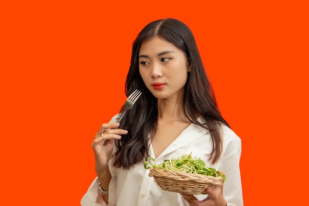 Concepto vegetariano Mujer sana comiendo brotes de girasol de pie aislado sobre fondo naranja