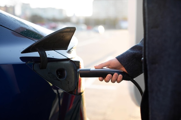 Concepto de vehículo eléctrico energía alternativa ecológica verde Mano de hombre de negocios con conector de alimentación para cargar el coche eléctrico