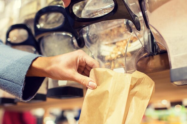 concepto de venta, compras y alimentos ecológicos: cierre de la mano femenina que vierte nueces en una bolsa de papel en la tienda de comestibles