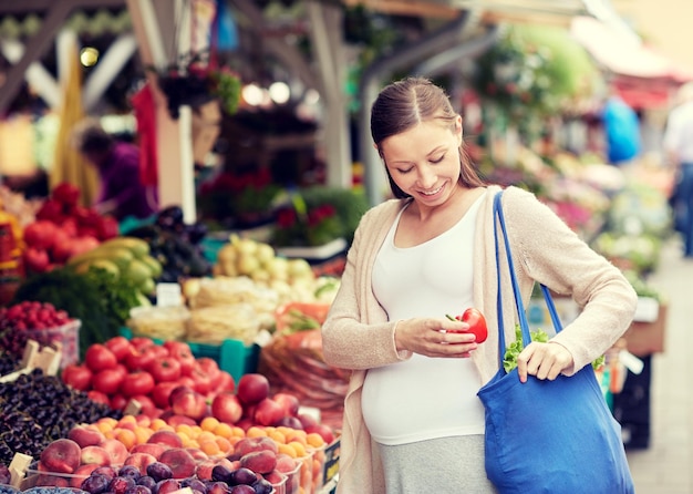 concepto de venta, compras, comida, embarazo y personas - mujer embarazada feliz comprando pimiento rojo o paprika en el mercado callejero