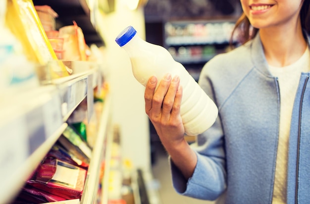 Foto concepto de venta, compras, consumismo, comida y personas - cerca de una joven feliz sosteniendo una botella de leche en el mercado