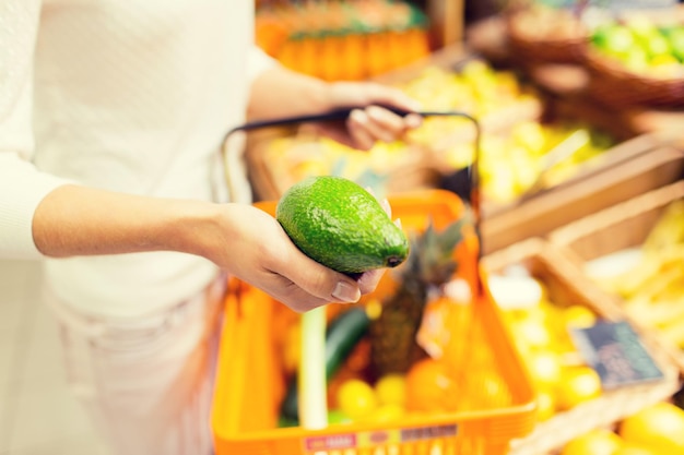 concepto de venta, compras, consumismo y personas - cierre de una mujer joven con canasta de alimentos y aguacate en el mercado