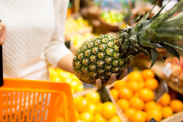 concepto de venta, compras, consumismo y personas - cierre de una mujer joven con canasta de alimentos y piña en el mercado de comestibles