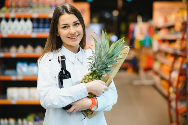 Concepto de venta, compras, consumismo y personas - mujer con canasta de alimentos en la tienda de comestibles o supermercado