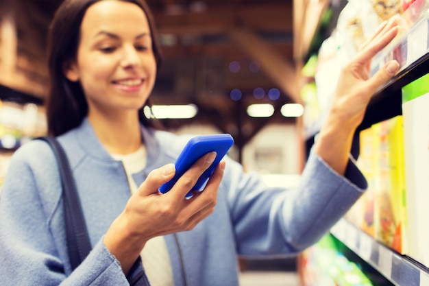 concepto de venta, compras, consumismo y personas - mujer joven feliz con smartphone eligiendo y comprando comida en el mercado