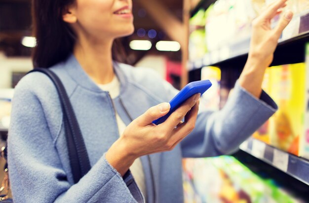 concepto de venta, compras, consumismo y personas - mujer joven feliz con smartphone eligiendo y comprando comida en el mercado