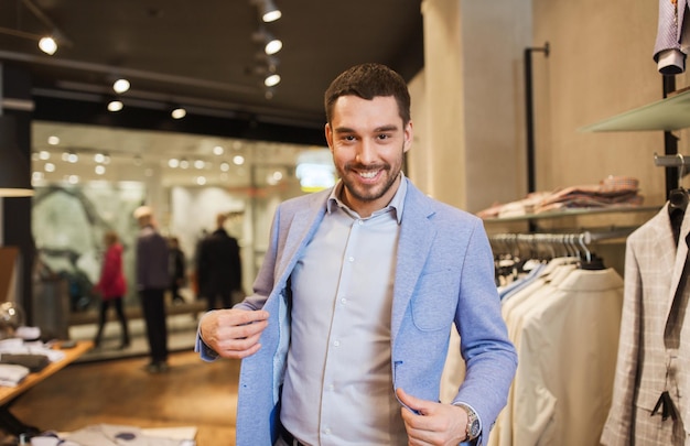 Foto concepto de venta, compras, moda, estilo y personas - joven elegante eligiendo y probando chaqueta en un centro comercial o tienda de ropa