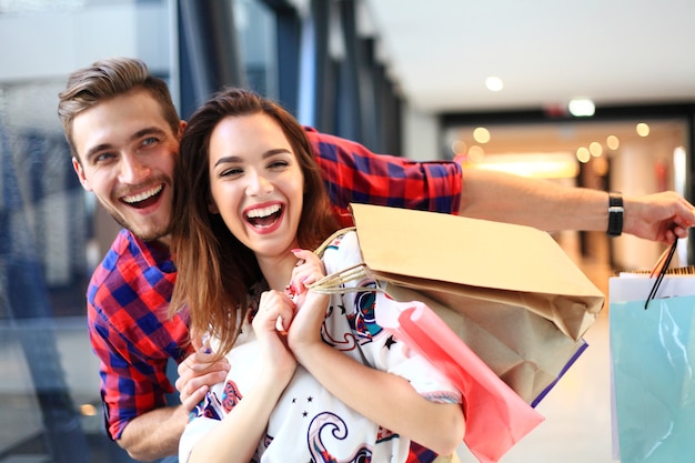 Foto concepto de venta, consumismo y personas - feliz pareja joven con bolsas de compras caminando en el centro comercial.