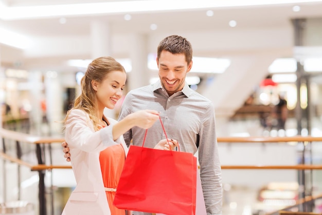 concepto de venta, consumismo y personas - feliz pareja joven mostrando contenido de bolsas de compras en el centro comercial