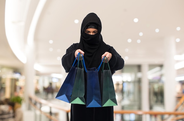 concepto de venta, consumismo y personas - mujer musulmana en hiyab con bolsas de compras sobre el fondo del centro comercial