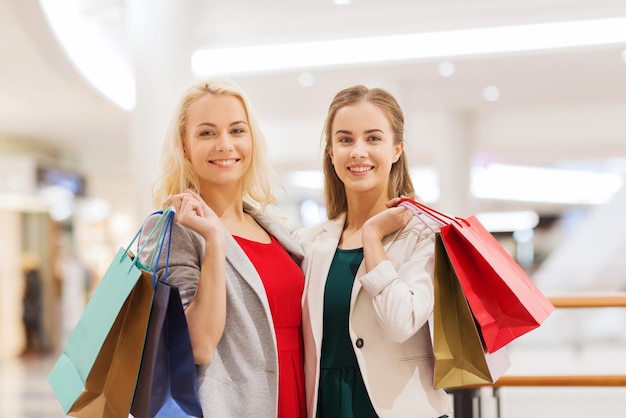 concepto de venta, consumismo y personas - mujeres jóvenes felices con bolsas de compras en el centro comercial