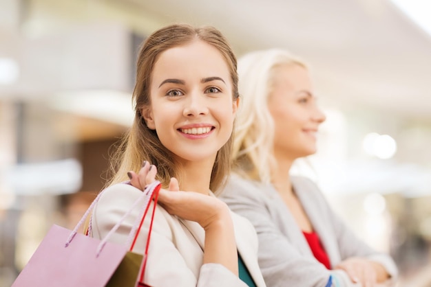 concepto de venta, consumismo y personas - mujeres jóvenes felices con bolsas de compras en el centro comercial