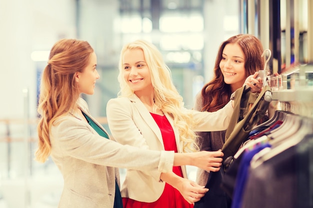 concepto de venta, consumismo y personas - mujeres jóvenes felices eligiendo ropa en el centro comercial